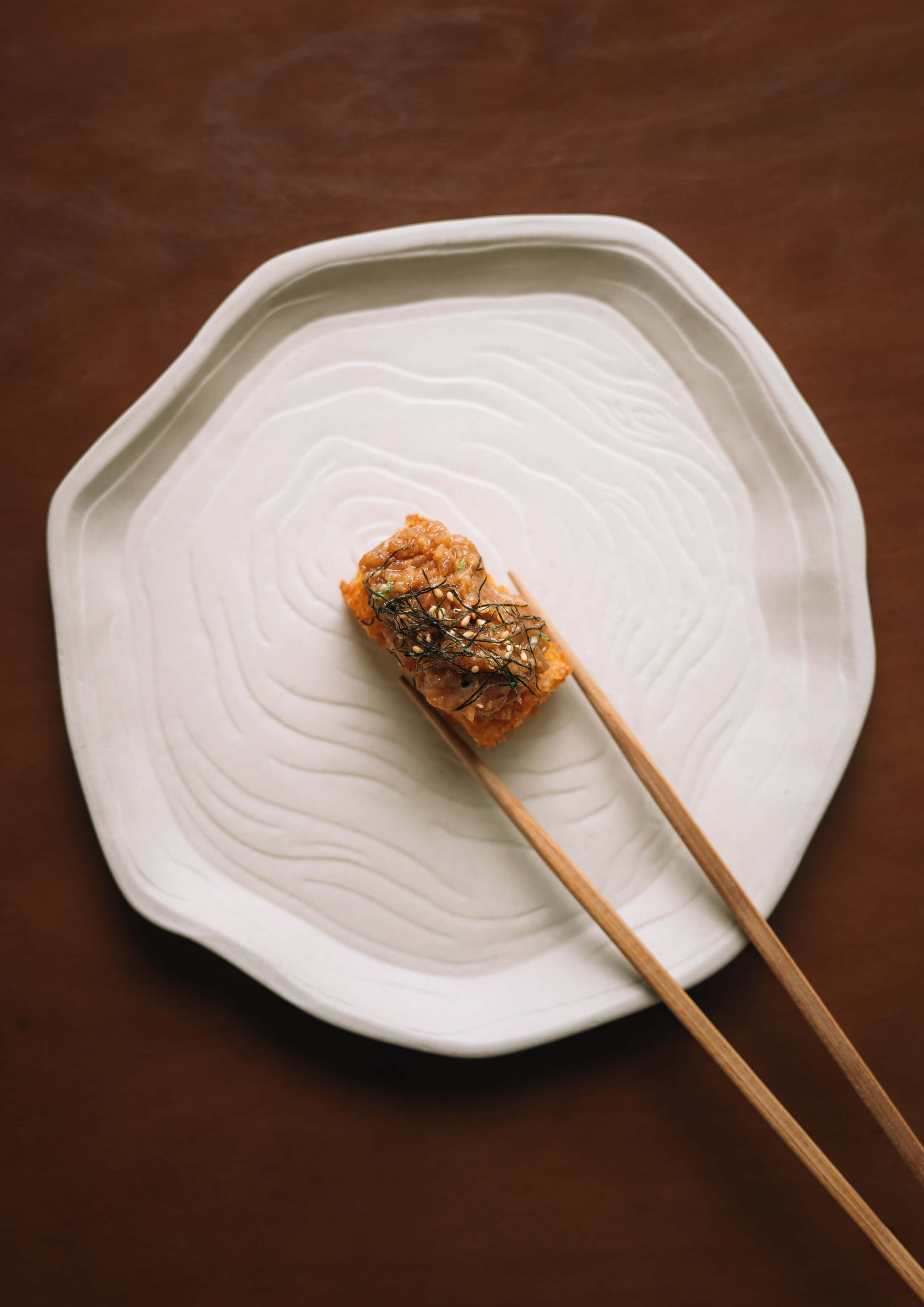 Sushi roll on a white plate with chopsticks on a wooden surface