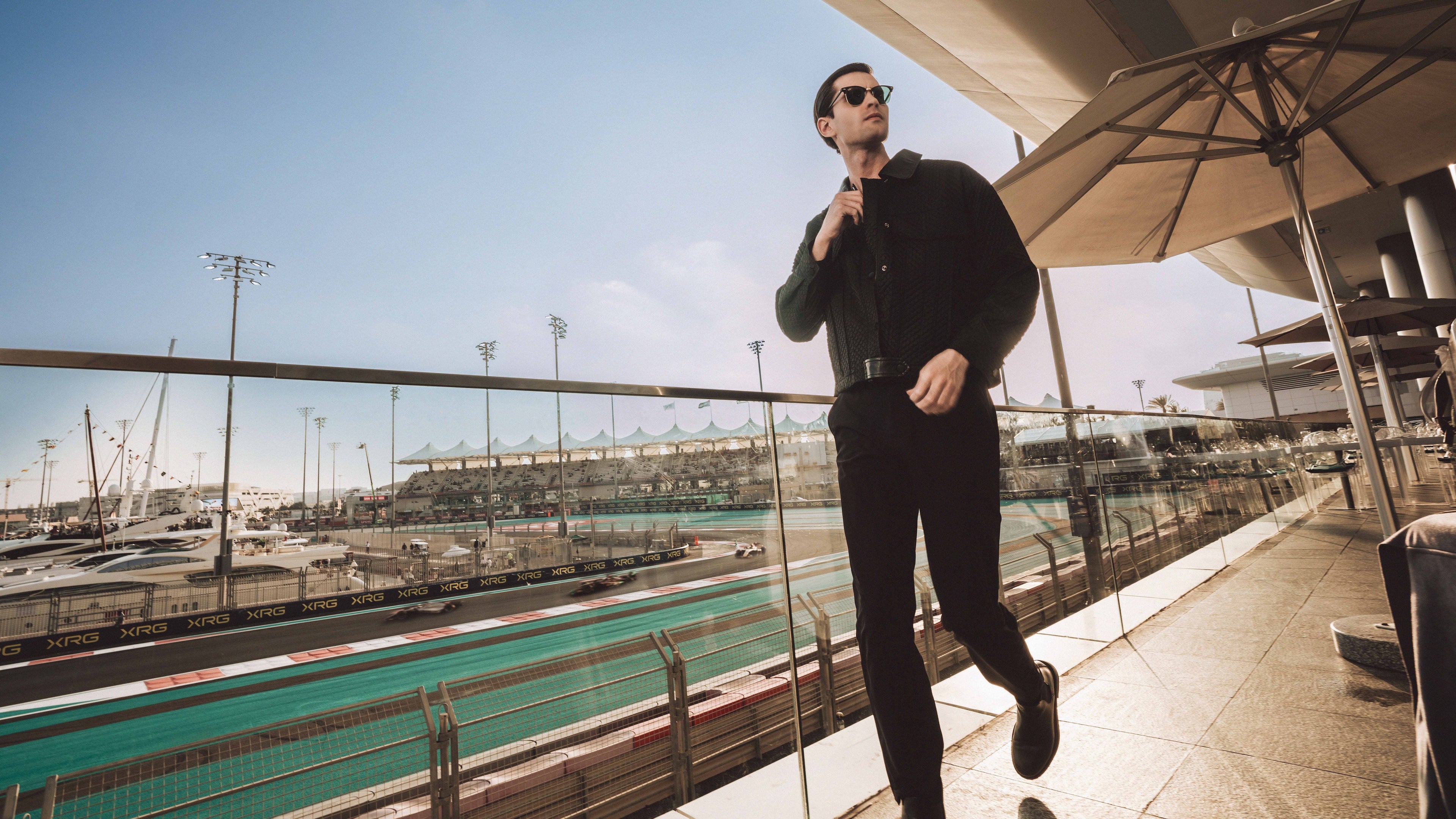 Man walking on a balcony overlooking a race track with clear blue sky