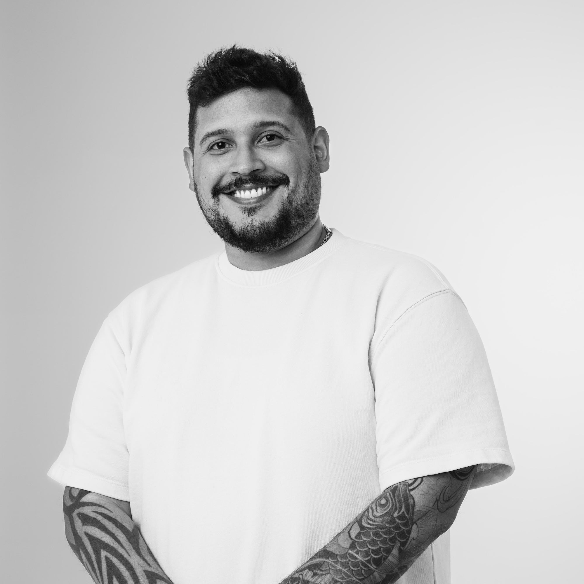Man wearing a white t-shirt with tattoos on arms against a plain background